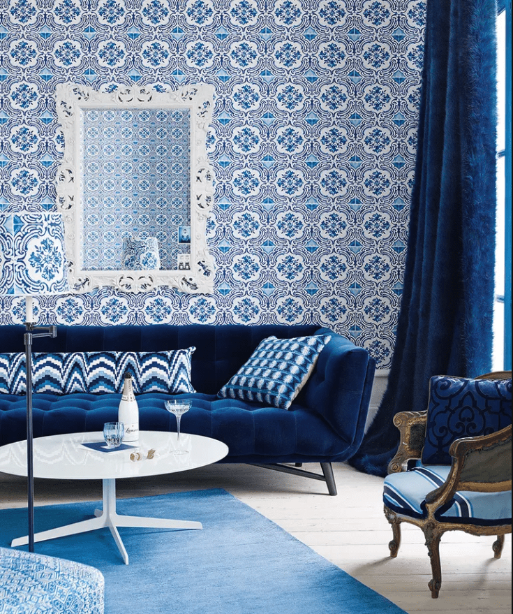 A room with blue tiles on the wall, a blue couch, blue rug, blue curtains, and accents